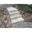 Illustration: Foto einer vierstufigen Treppe aus Beton, die von großen Natursteinen eingefasst ist und von einer runden, gepfasterten Fläche auf einen gepflasterten Weg führt