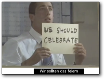 Scene from “Signs”:  Man looks into the far and holds a handwritten sign with the text: “WE SHOULD CELEBRATE”, subtitled to “Wir sollten das feiern“.