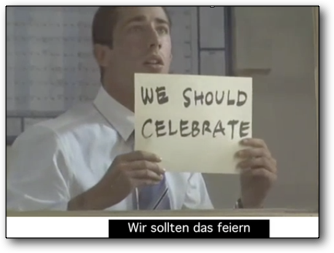 Szene aus „Signs“: Mann sieht in die Ferne und hält ein handgeschriebenes Blatt mit dem Text „WE SHOULD CELEBRATE“, untertitelt zu „Wir sollten das feiern“.